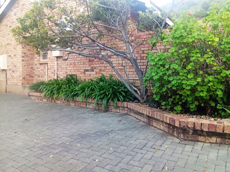 A rear exterior view of the townhouse featuring a brick paved courtyard area with a built-in brick retaining wall and established garden beds.