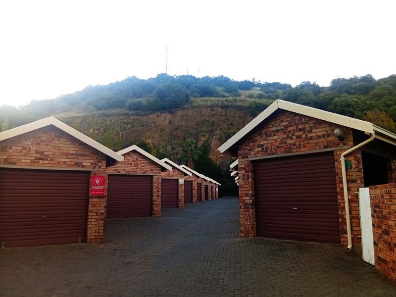 A row of brick-constructed garages with roller shutter doors and paved driveway access, set against a hillside backdrop.