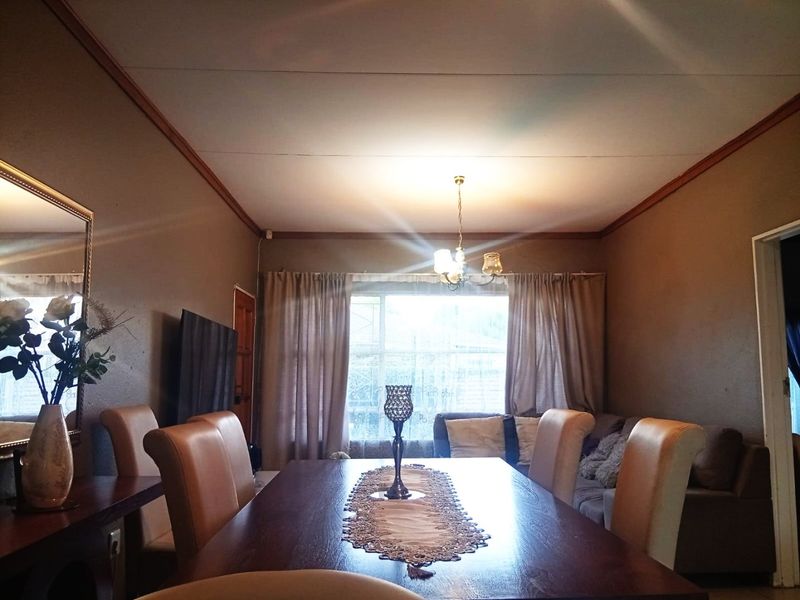 A dining room featuring a central pendant light fixture, large window with curtains, and decorative ceiling cornicing.