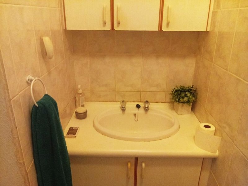 A compact bathroom featuring a built-in vanity with a ceramic basin, wall-mounted storage cabinets, and full-height wall tiling.
