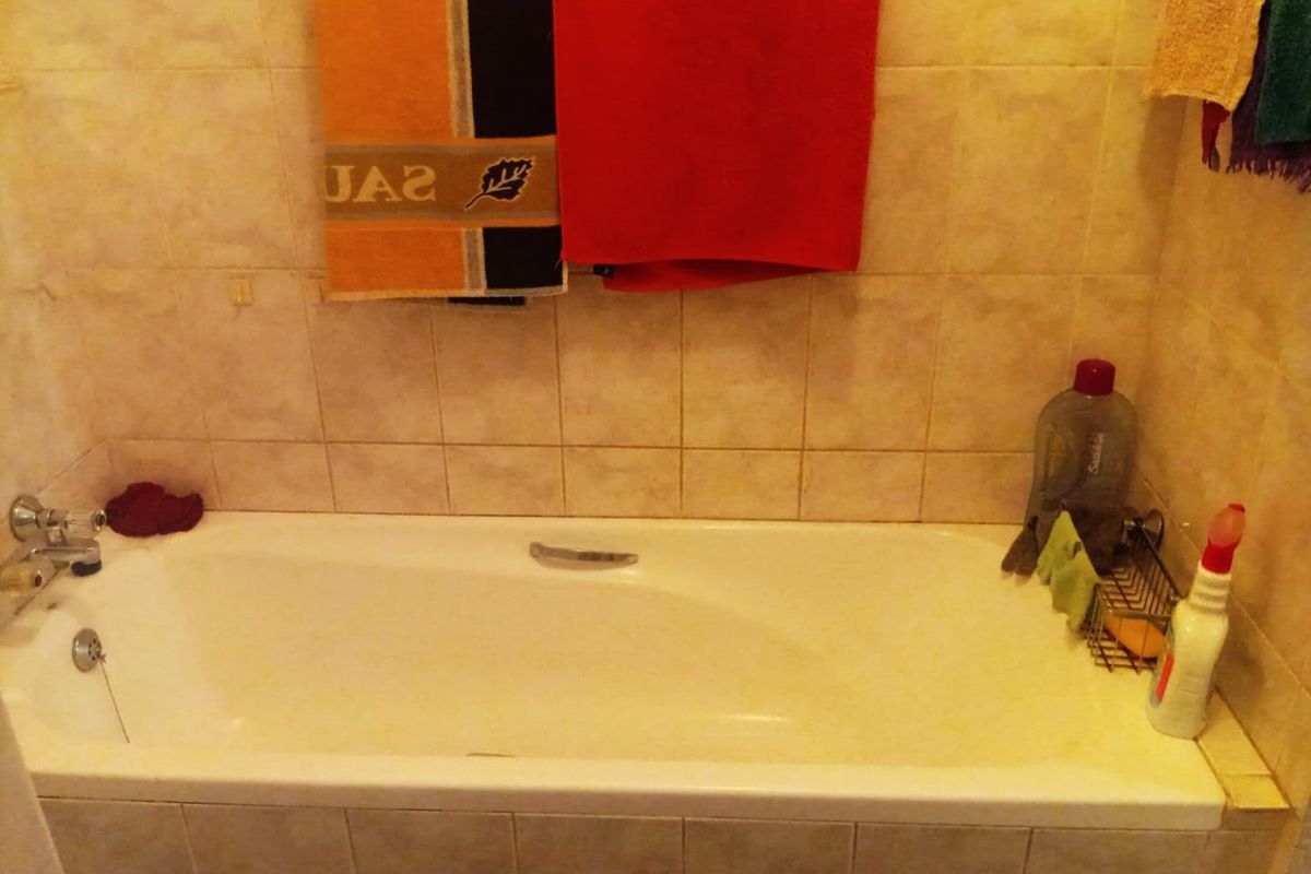 A standard bathroom featuring a built-in bathtub with chrome fixtures and neutral ceramic wall tiling.
