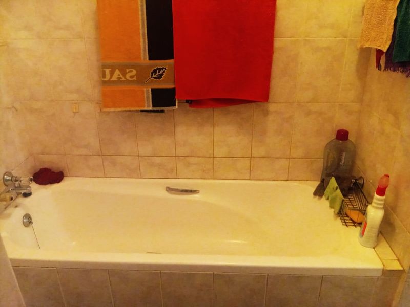 A standard bathroom featuring a built-in bathtub with chrome fixtures and neutral ceramic wall tiling.
