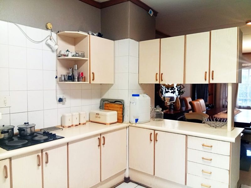A functional kitchen featuring laminate cabinetry, tiled backsplash, and a built-in gas hob, offering a practical layout with potential for modern cosmetic updates.