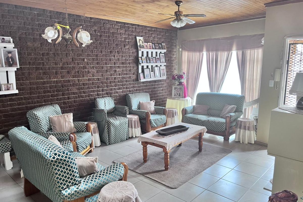 Spacious living room featuring a distinctive exposed brick wall, timber ceiling, and tiled flooring, offering a classic and comfortable living space.