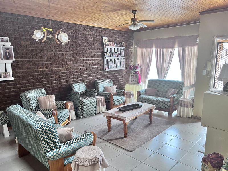 Spacious living room featuring a distinctive exposed brick wall, timber ceiling, and tiled flooring, offering a classic and comfortable living space.