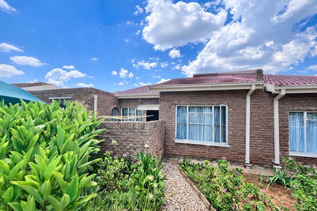 Rear view of a face brick townhouse featuring a tiled roof, aluminium window frames with security bars, and a landscaped garden with a paved pathway.