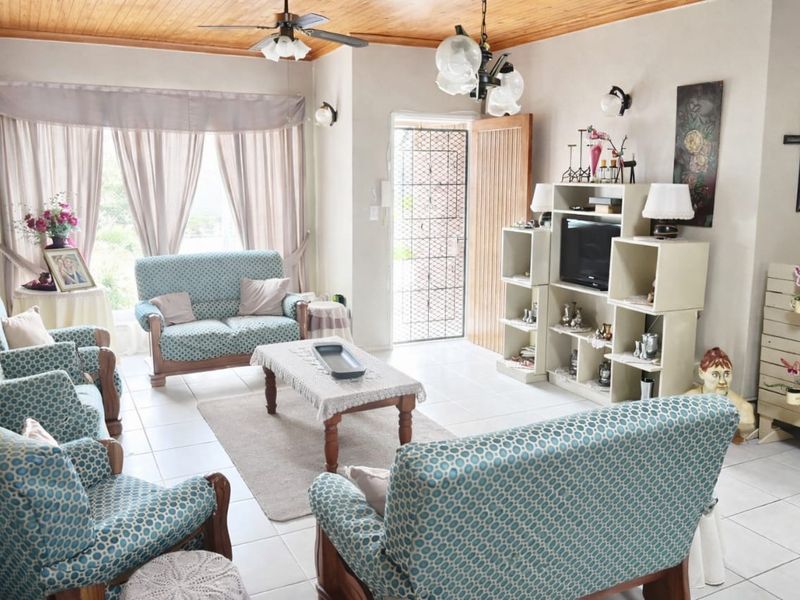 A comfortable living room featuring tiled flooring, a timber-paneled ceiling with a ceiling fan, and a security gate leading to the exterior.