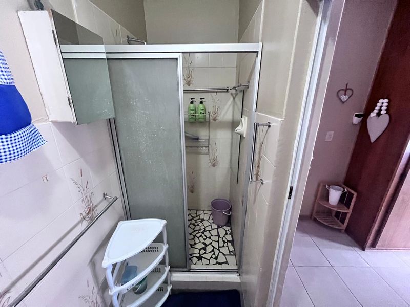 A compact bathroom featuring a shower enclosure with tiled walls and flooring, requiring some cosmetic updates to modernize the space.