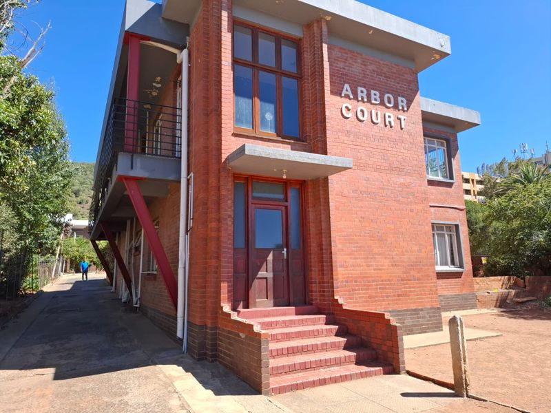 Exterior view of Arbor Court apartment building featuring a classic red brick facade, concrete balcony, and a raised brick entrance staircase.