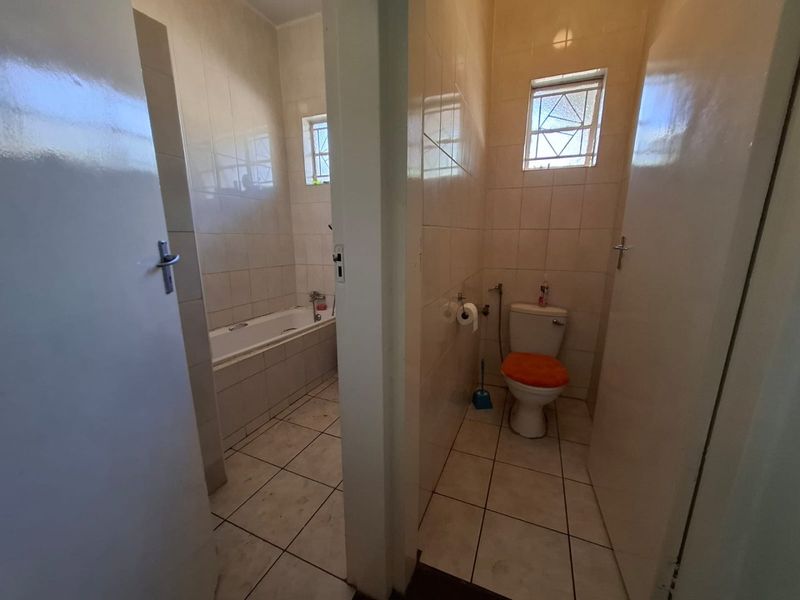 A dated bathroom featuring a separate bathtub and toilet area with tiled finishes, requiring cosmetic updates to improve its overall condition and appeal.