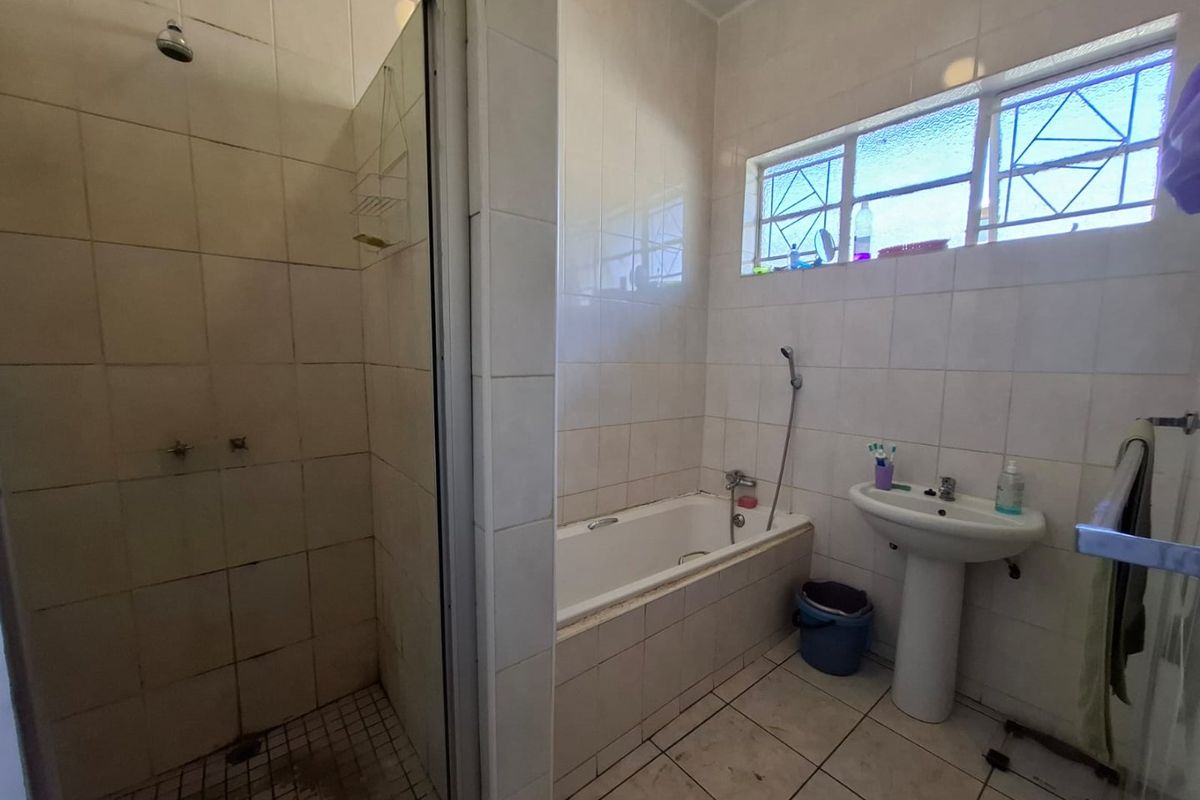 A functional bathroom featuring a separate shower enclosure, built-in bathtub, and pedestal basin, finished with neutral wall and floor tiling.