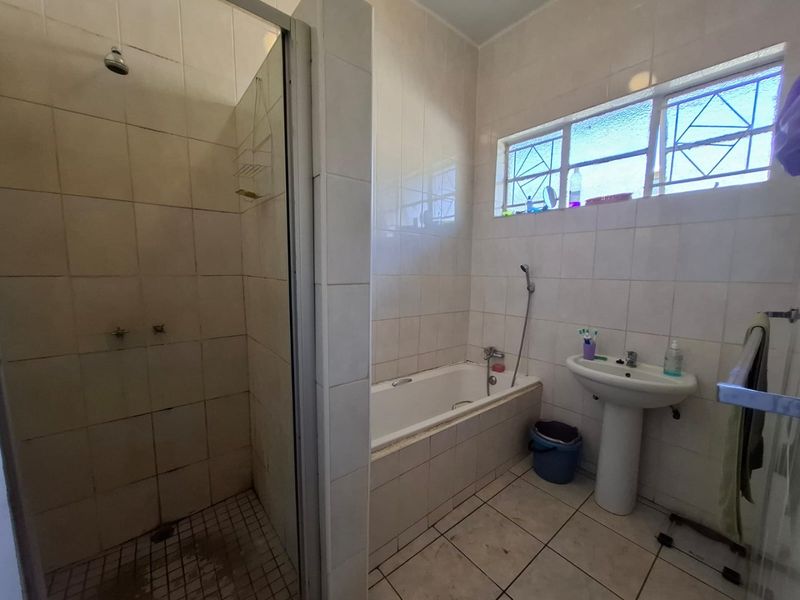 A functional bathroom featuring a separate shower enclosure, built-in bathtub, and pedestal basin, finished with neutral wall and floor tiling.