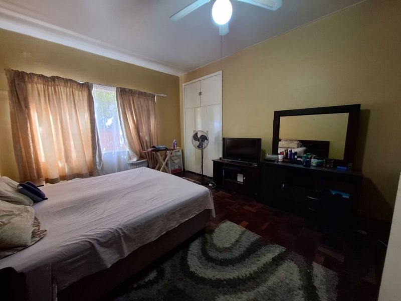 A spacious bedroom featuring original parquet flooring, built-in cupboards, and a ceiling fan, offering a functional layout with potential for cosmetic updates.