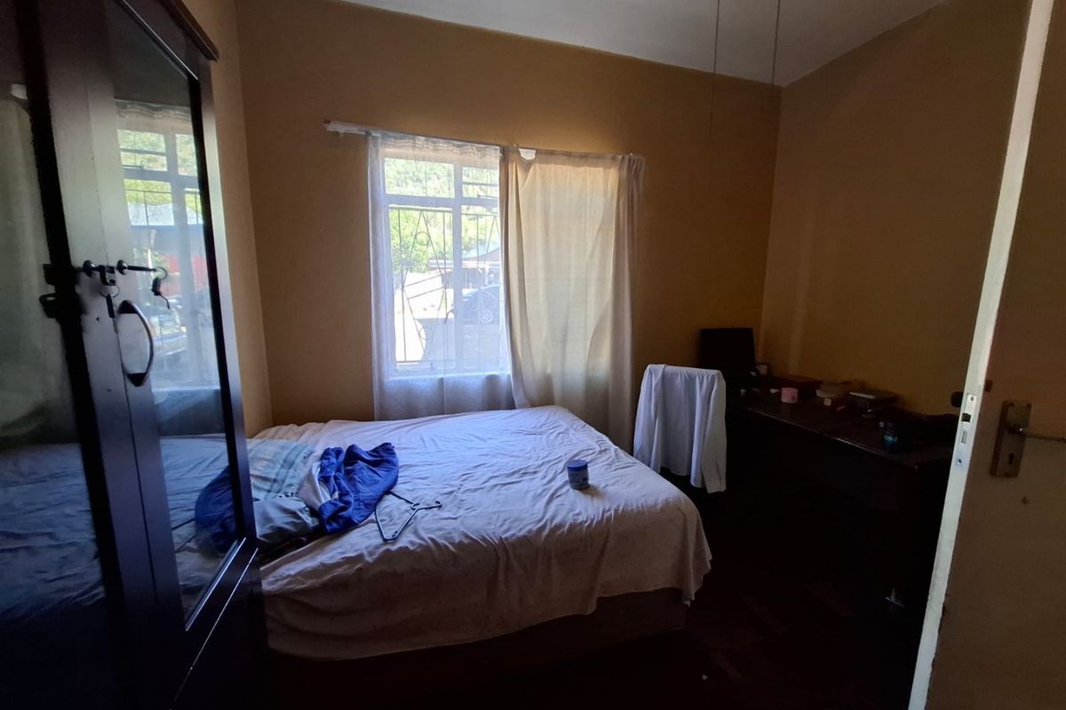 A bedroom featuring parquet flooring and security bars on the window, requiring cosmetic updates to improve the overall aesthetic.