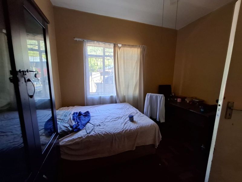 A bedroom featuring parquet flooring and security bars on the window, requiring cosmetic updates to improve the overall aesthetic.
