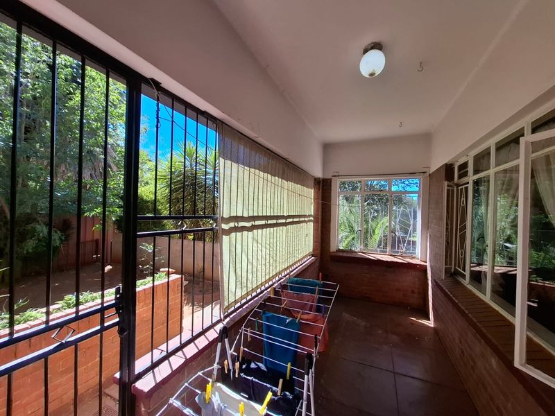 A covered patio area featuring tiled flooring, brick wall accents, and security gates, providing a functional outdoor space with garden views.