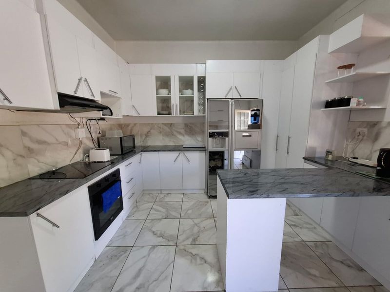 Modern kitchen featuring white cabinetry, marble-look countertops, tiled flooring, and a functional breakfast bar layout with integrated oven and hob.