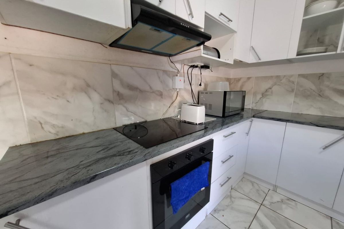 A compact kitchen featuring white cabinetry, stone countertops, marble-look backsplash, and integrated appliances including an oven and hob.