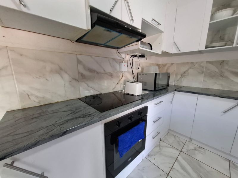 A compact kitchen featuring white cabinetry, stone countertops, marble-look backsplash, and integrated appliances including an oven and hob.