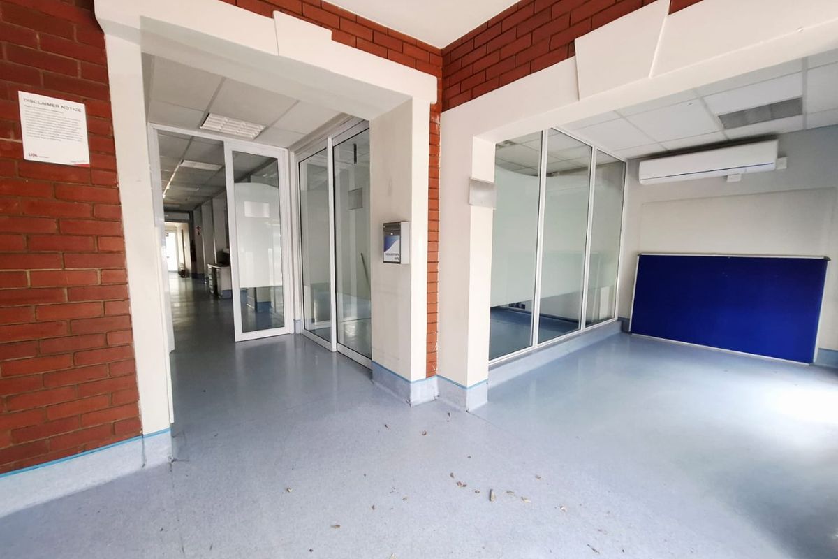 A commercial hallway featuring exposed brick walls, glass partitions, and vinyl flooring, providing a clean and functional layout for office or clinical use.