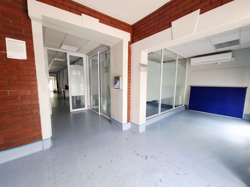 A commercial hallway featuring exposed brick walls, glass partitions, and vinyl flooring, providing a clean and functional layout for office or clinical use.