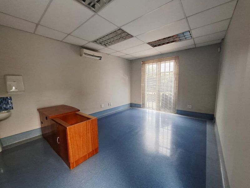 A functional, empty office space featuring vinyl flooring, a suspended ceiling with recessed lighting, a wall-mounted basin, and a split-system air conditioner.