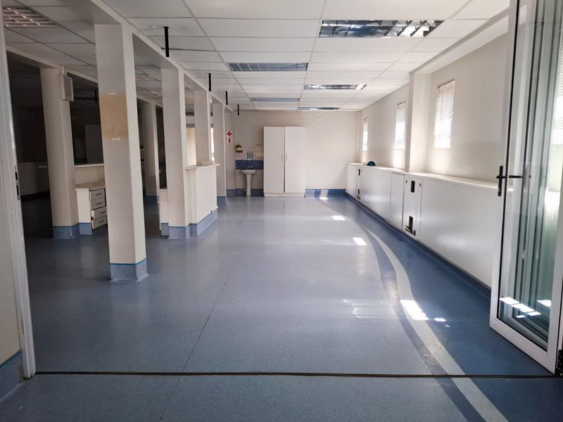 Spacious open-plan commercial interior featuring durable vinyl flooring, suspended ceilings, structural columns, and a functional built-in sink and cabinetry area.