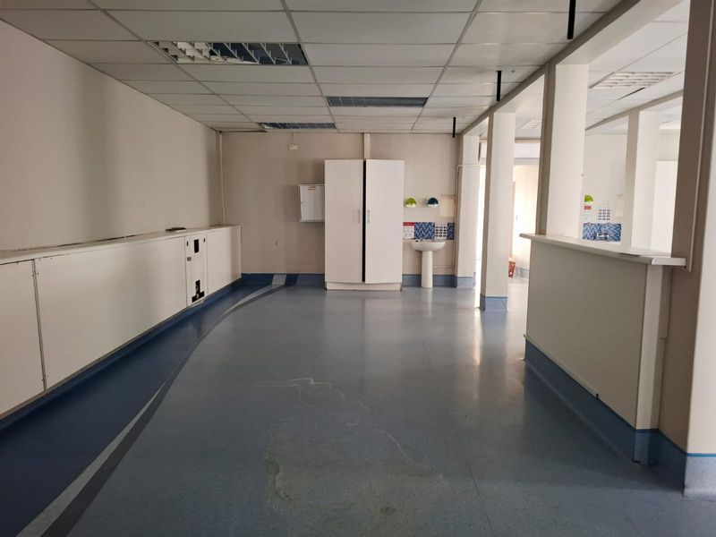 An empty commercial utility space featuring vinyl flooring, a pedestal sink with tiled splashback, and built-in cabinetry under a suspended ceiling.