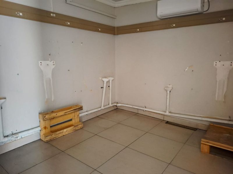 An empty utility space featuring tiled flooring, exposed plumbing, and a wall-mounted air conditioning unit, requiring cosmetic refurbishment.