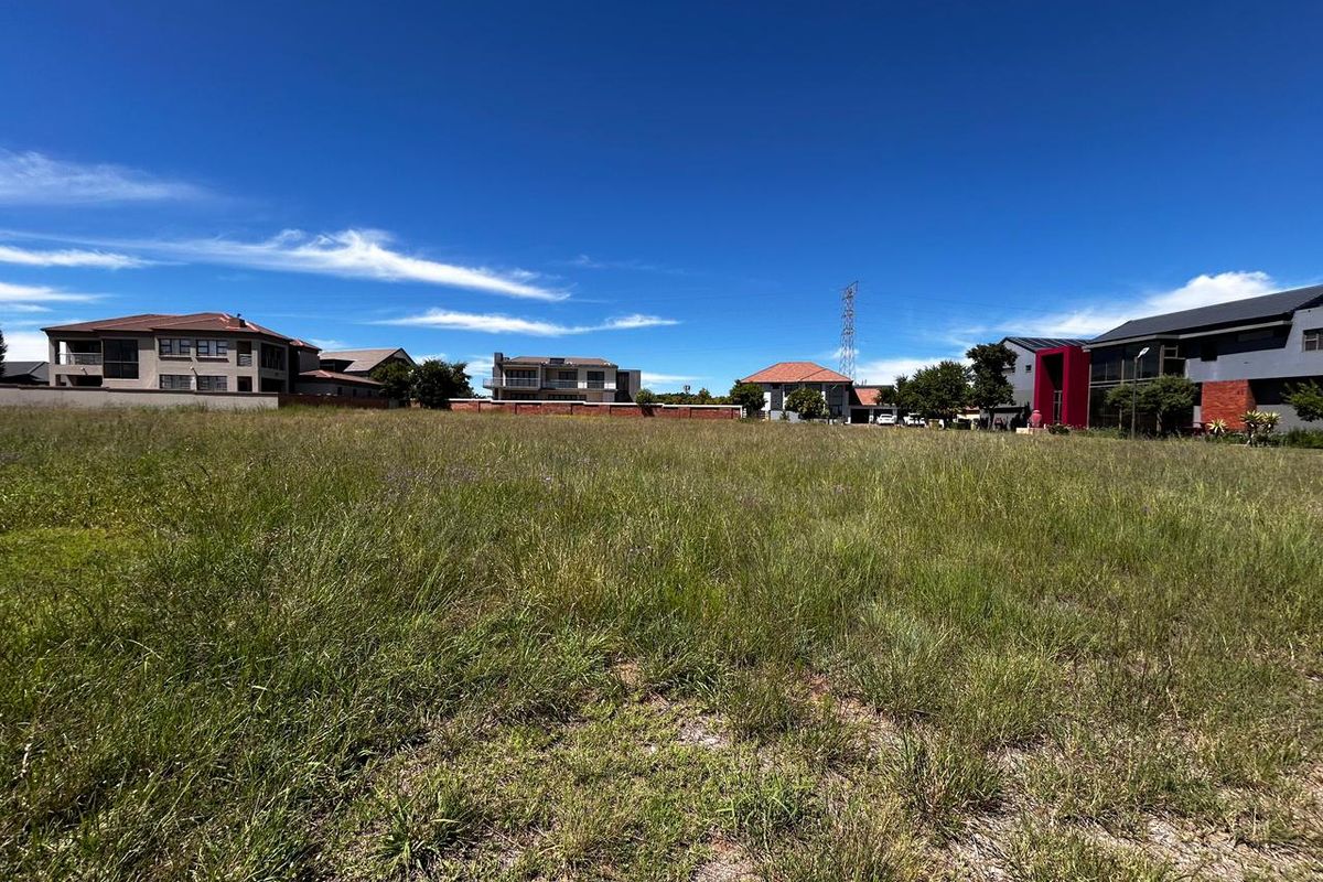 A vacant residential plot of land featuring natural grass cover, situated within an established neighborhood with surrounding residential properties.