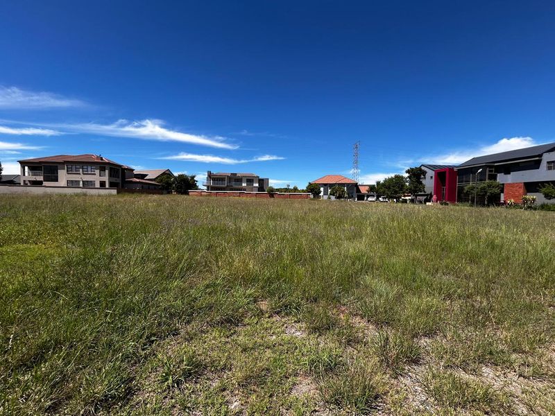 A vacant residential plot of land featuring natural grass cover, situated within an established neighborhood with surrounding residential properties.