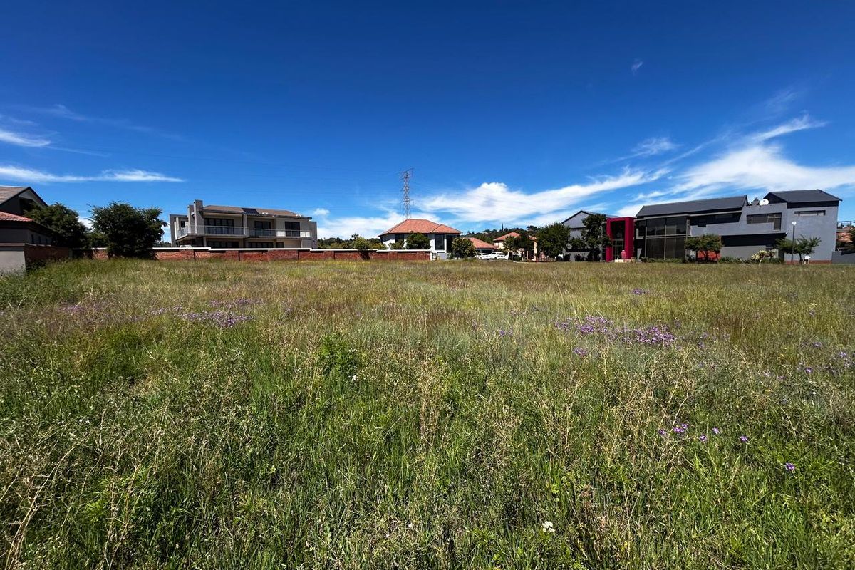 A wide-angle view of a vacant residential plot featuring natural grass coverage and a perimeter brick wall, situated within an established residential neighborhood.