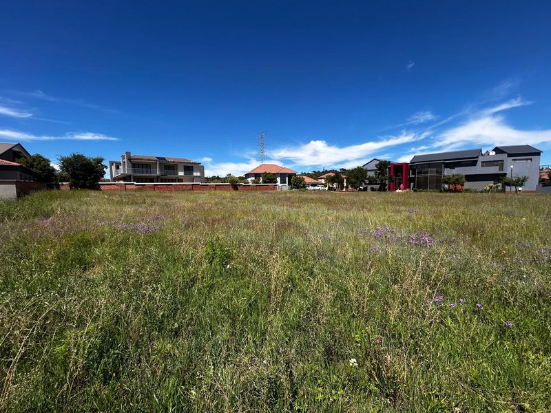 A wide-angle view of a vacant residential plot featuring natural grass coverage and a perimeter brick wall, situated within an established residential neighborhood.