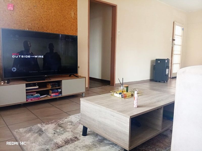 A living room featuring tiled flooring and a distinctive cork feature wall, providing a neutral base for potential interior updates.