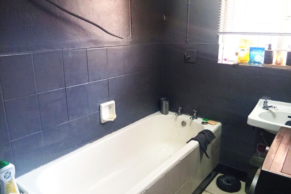 A bathroom featuring dark tiled walls, a standard bathtub, and a basin. The space requires cosmetic updates and maintenance to improve its overall condition.