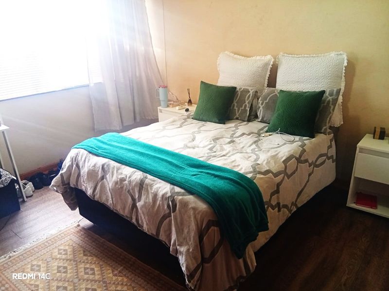 A bedroom featuring laminate flooring and window blinds, providing a functional space for rest.