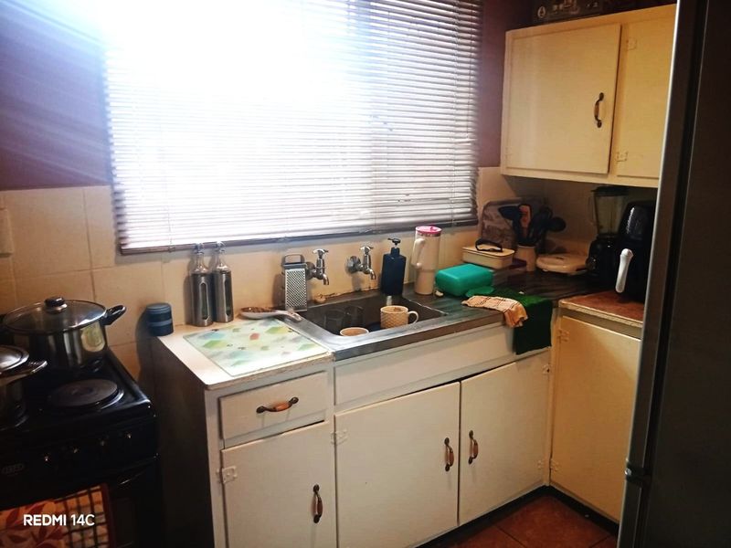 A compact, dated kitchen featuring original cabinetry, a stainless steel sink, and a tiled backsplash, offering significant potential for a modern renovation.