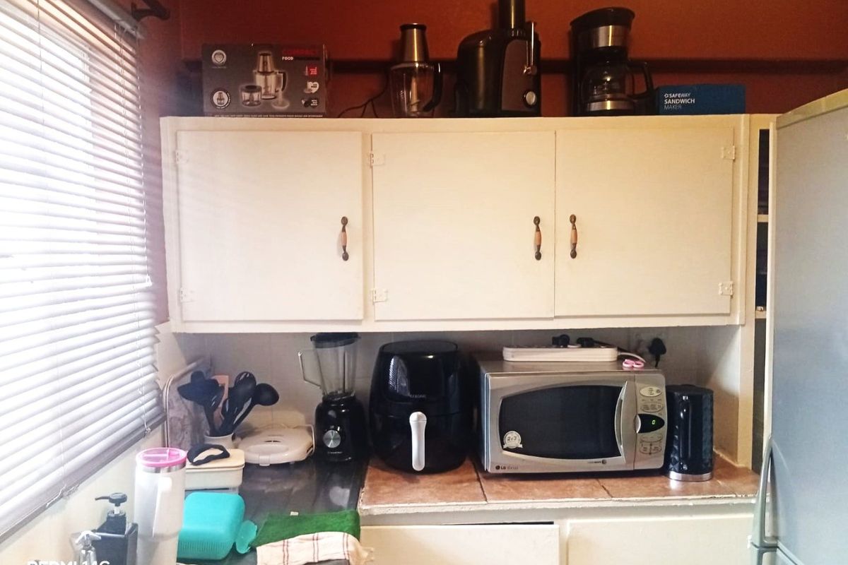 A compact kitchen area featuring built-in cabinetry, a tiled countertop, and a stainless steel sink, currently showing signs of age and wear.