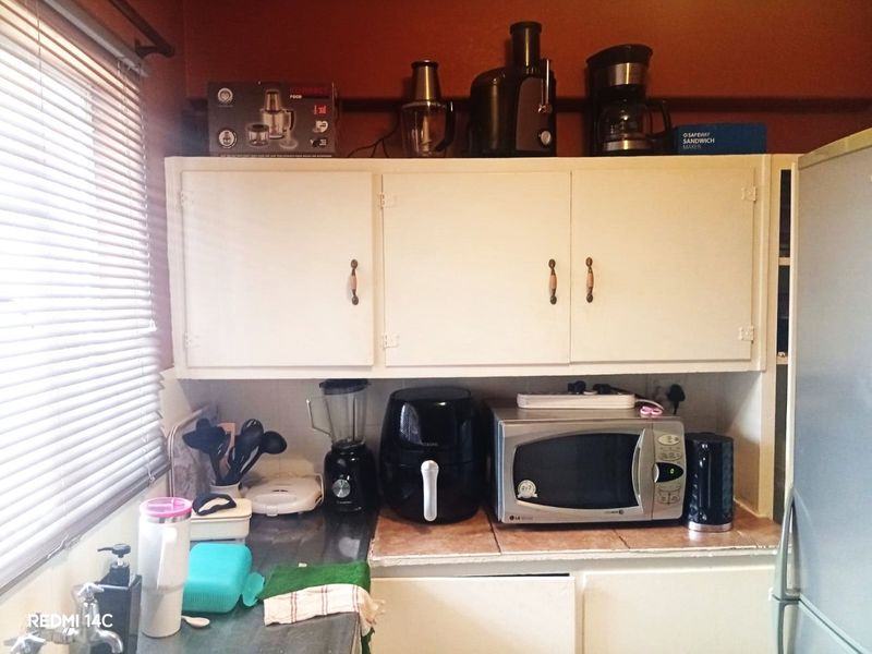 A compact kitchen area featuring built-in cabinetry, a tiled countertop, and a stainless steel sink, currently showing signs of age and wear.