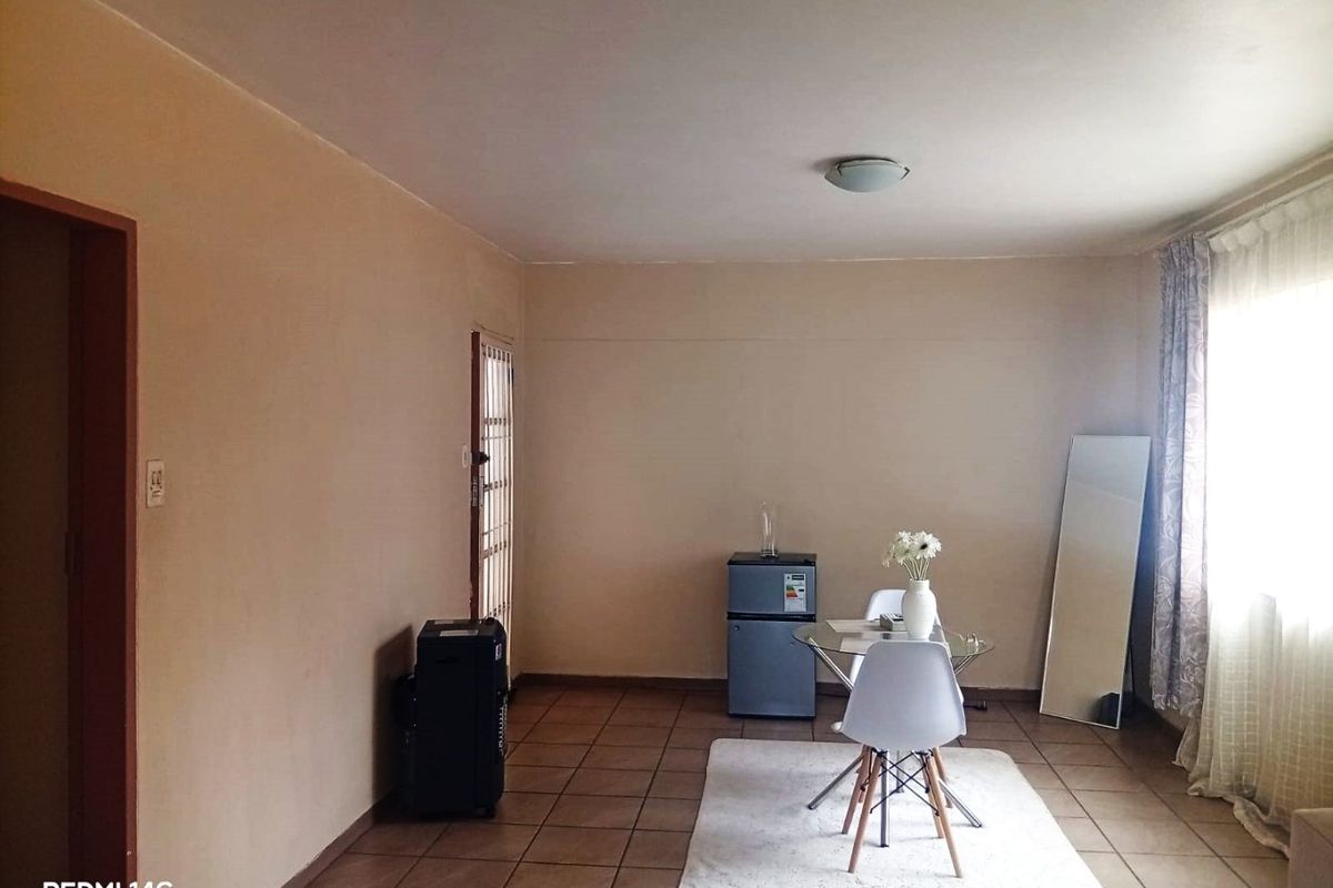 A simple living area featuring tiled flooring, a security gate, and neutral wall finishes, offering a functional space ready for personalization.