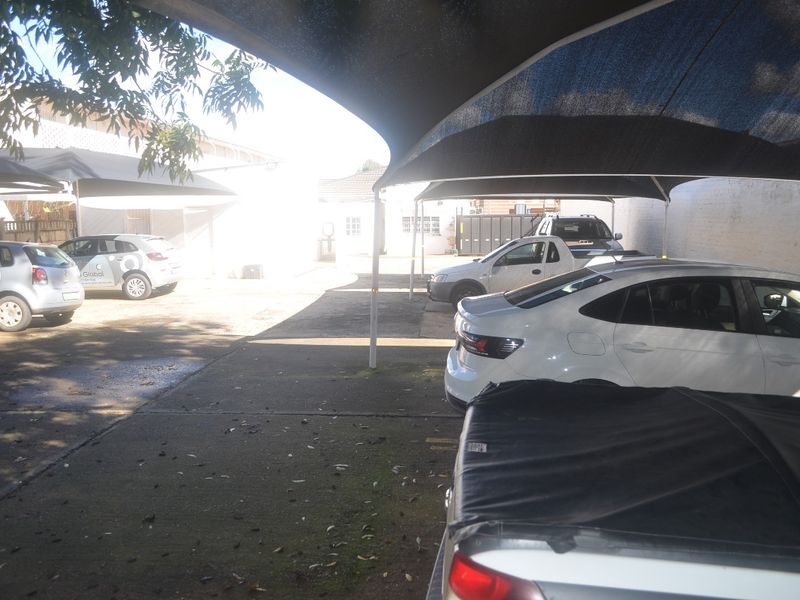 A paved outdoor parking area featuring multiple shade cloth carports and perimeter walling, providing functional covered vehicle storage for the commercial property.
