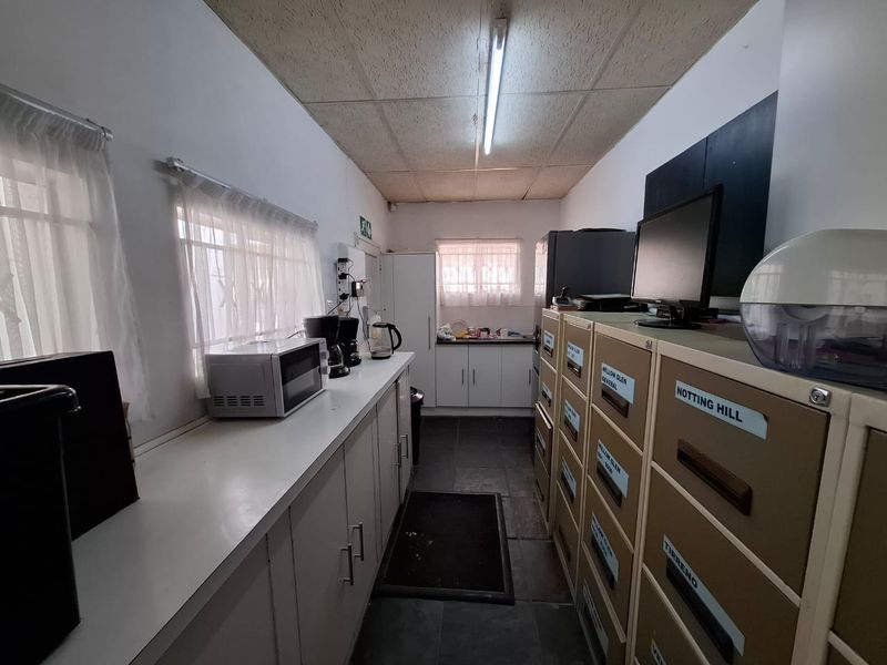 A functional utility or kitchenette area featuring built-in cabinetry, tiled flooring, and fluorescent lighting, suitable for office or commercial support use.