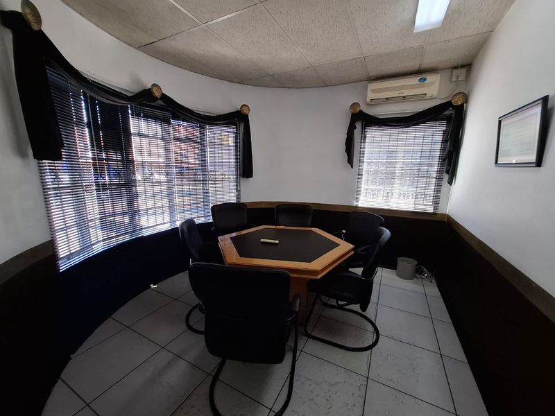 A compact office space featuring tiled flooring, a drop ceiling, and a wall-mounted air conditioning unit with curved window frontage.