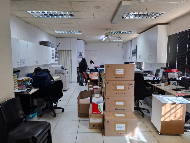 A functional commercial office space featuring built-in storage cabinetry, suspended ceiling tiles, and tiled flooring, currently utilized as a workspace.