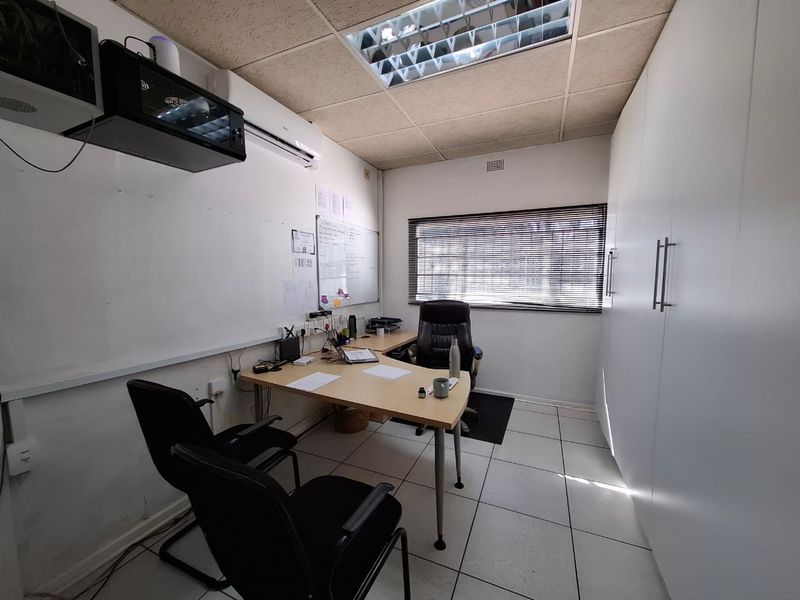 A functional commercial office space featuring tiled flooring, built-in storage cupboards, a drop ceiling with integrated lighting, and a wall-mounted air conditioning unit.