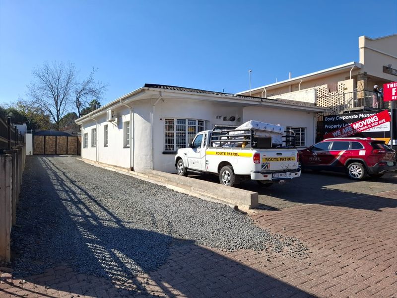 Front exterior view of a commercial property featuring a paved and gravel driveway, security gates, and exterior wall-mounted air conditioning units.