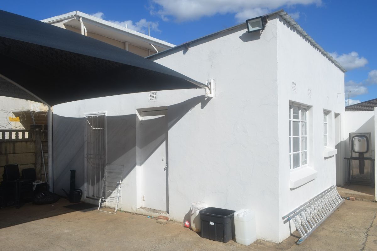 Rear exterior view of the commercial building featuring a shade sail, concrete paving, and security gate access.