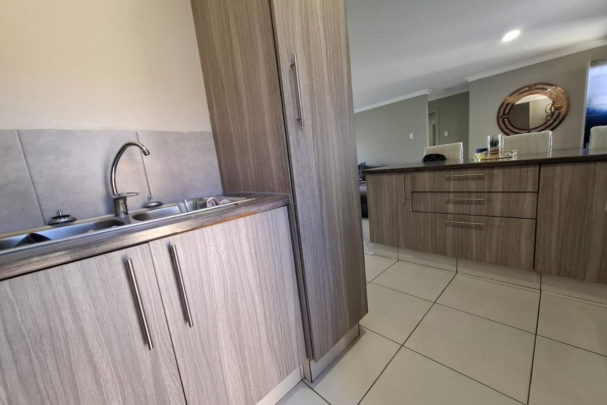 Modern kitchen featuring wood-grain cabinetry, tiled flooring, and a stainless steel sink with a mixer tap, seamlessly flowing into the adjacent living area.