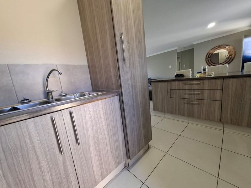 Modern kitchen featuring wood-grain cabinetry, tiled flooring, and a stainless steel sink with a mixer tap, seamlessly flowing into the adjacent living area.