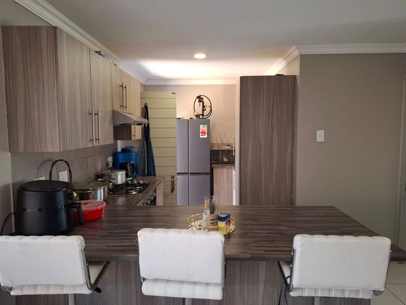 Modern kitchen featuring wood-grain cabinetry, laminate countertops, a breakfast bar, and integrated gas hob with extractor fan.